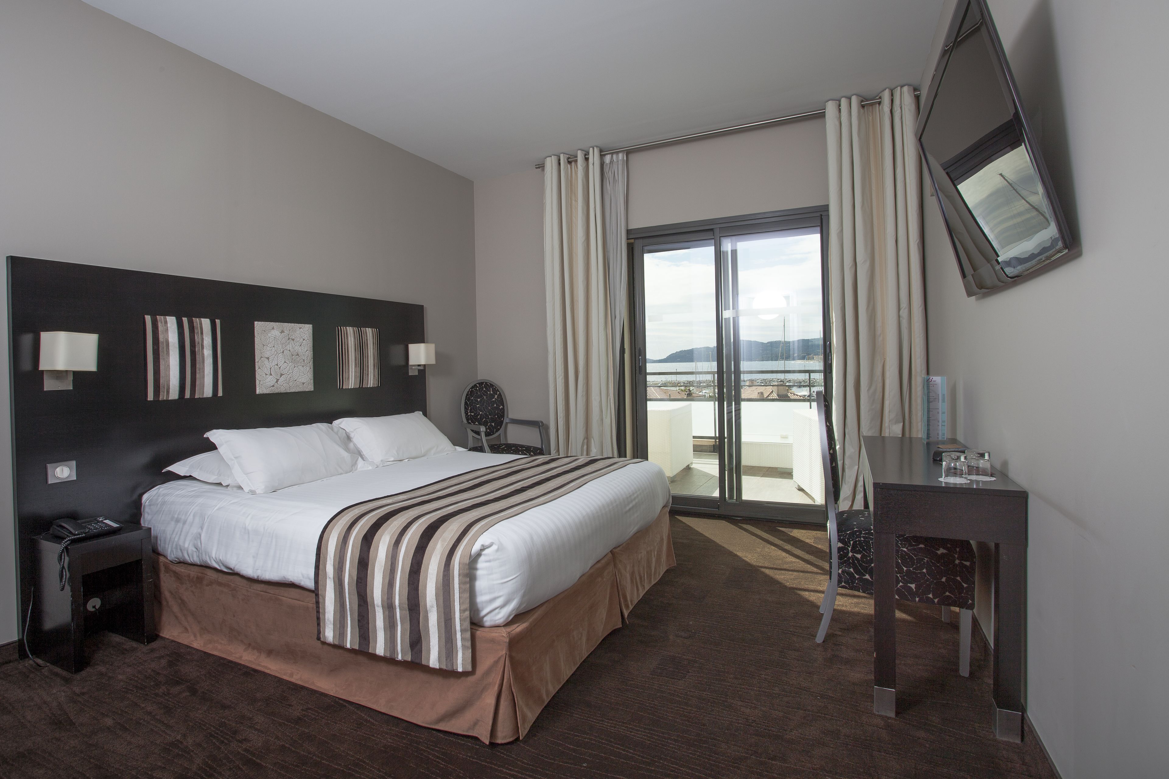 A hotel room with a large bed, a desk, a chair, a phone, and a view of the outdoors.
