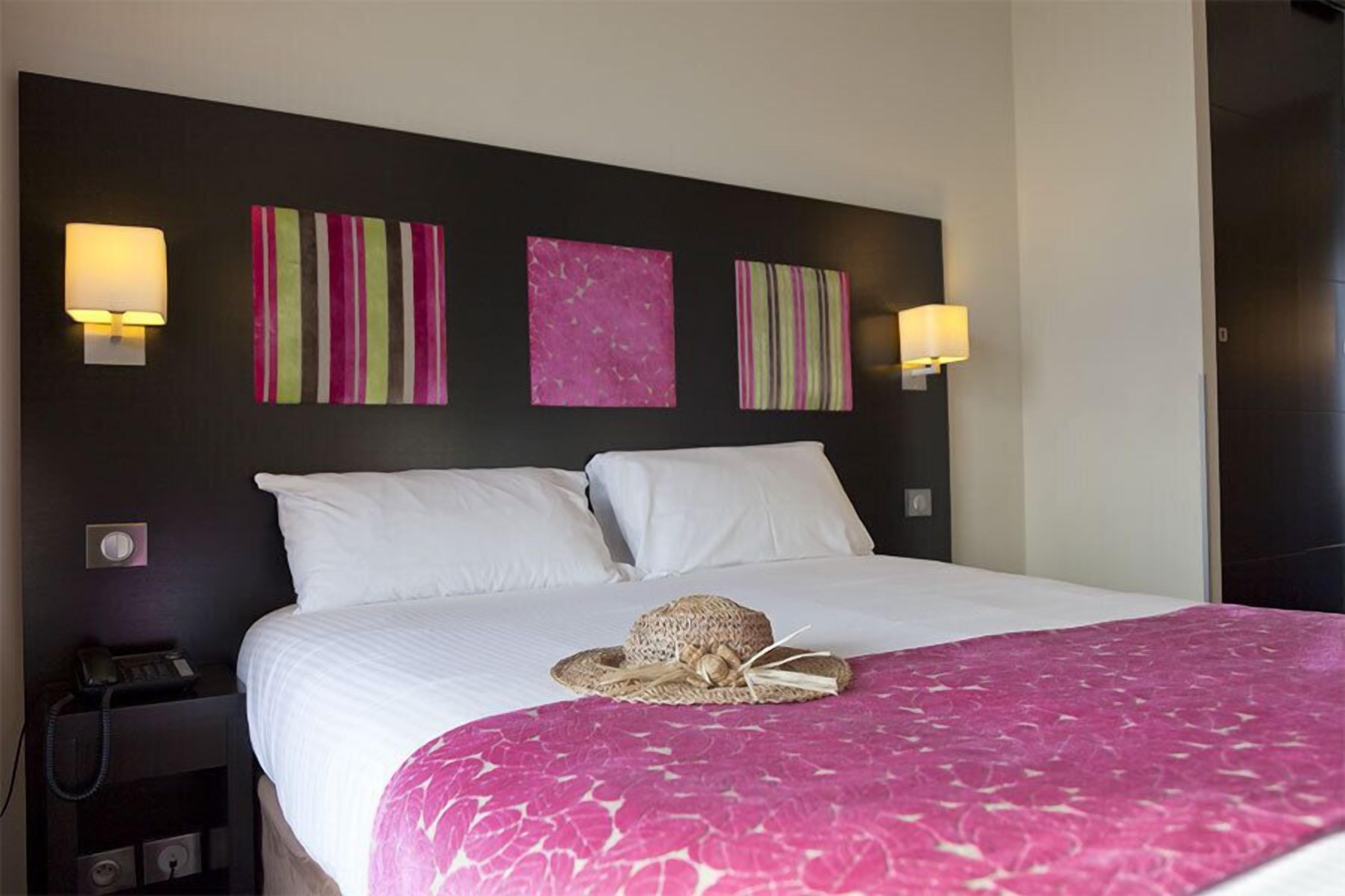 A hotel room with a large bed, two bedside lamps, a telephone, and artwork on the wall.