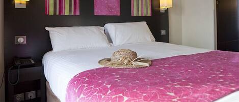 A hotel room with a large bed, two bedside lamps, a telephone, and artwork on the wall.