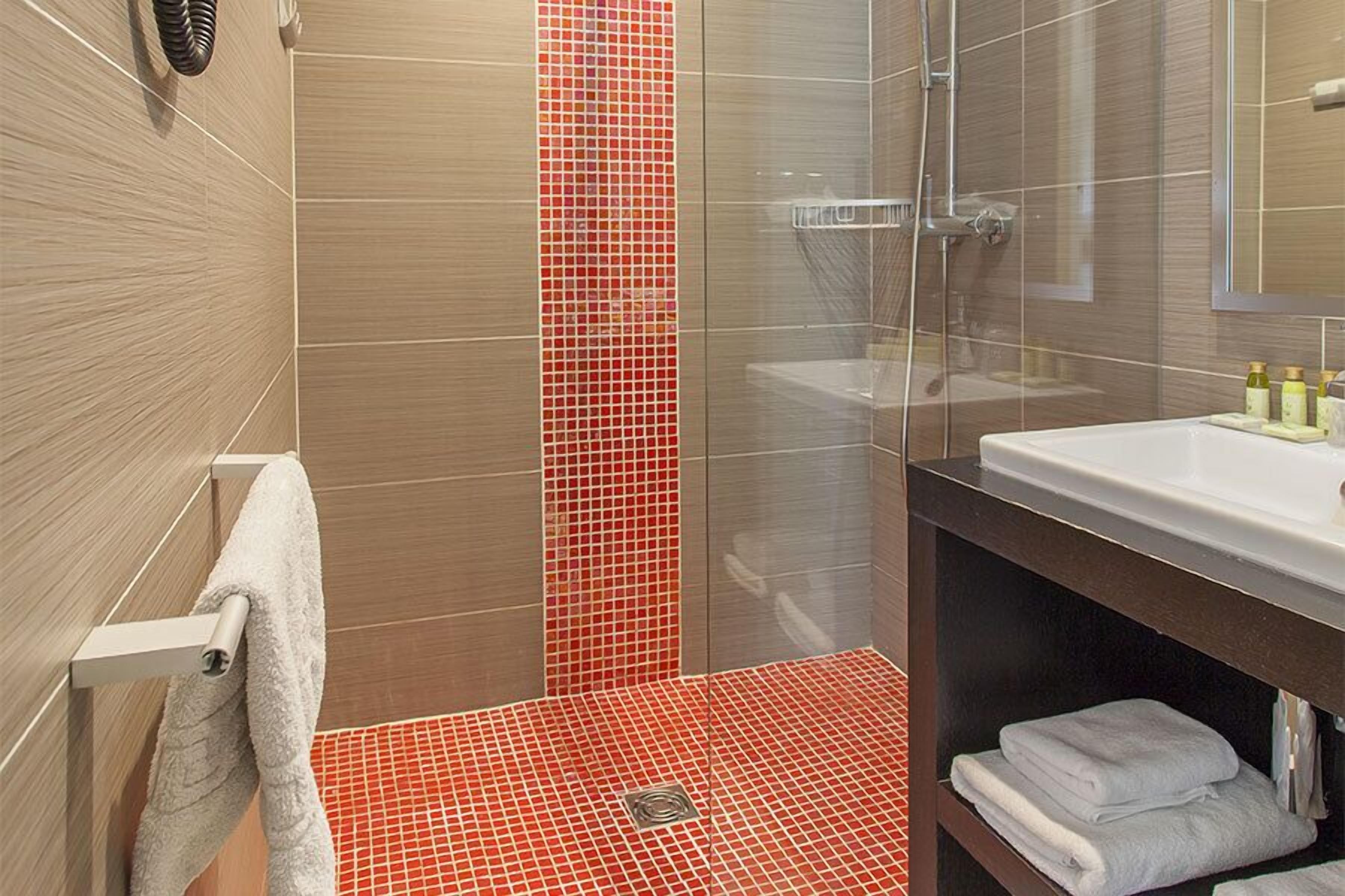 A modern bathroom with a glass shower enclosure, a white sink, and a shelf with folded towels.