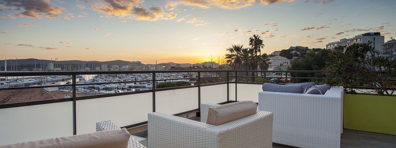 Un balcone con mobili in vimini e vista su un porto turistico al tramonto.