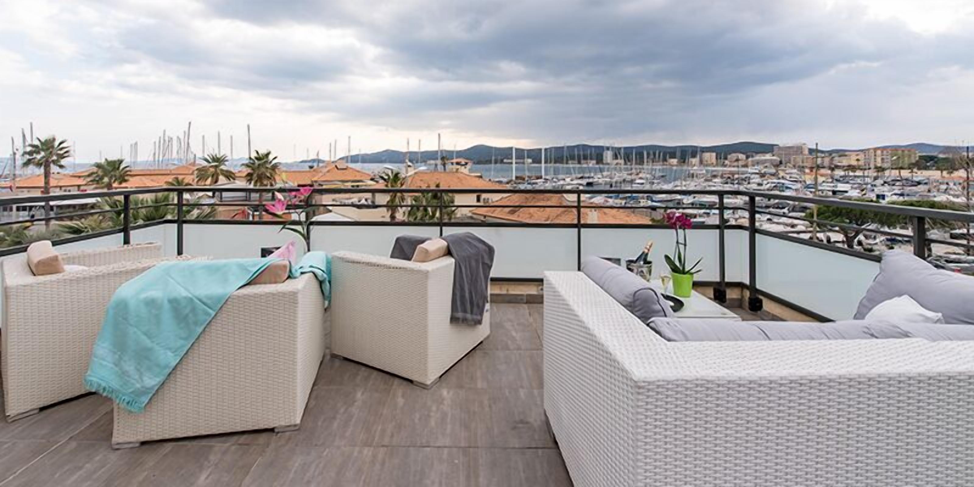 A balcony with wicker furniture, a view of a marina, and distant hills.