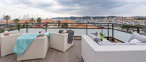 A balcony with wicker furniture, a view of a marina, and distant hills.
