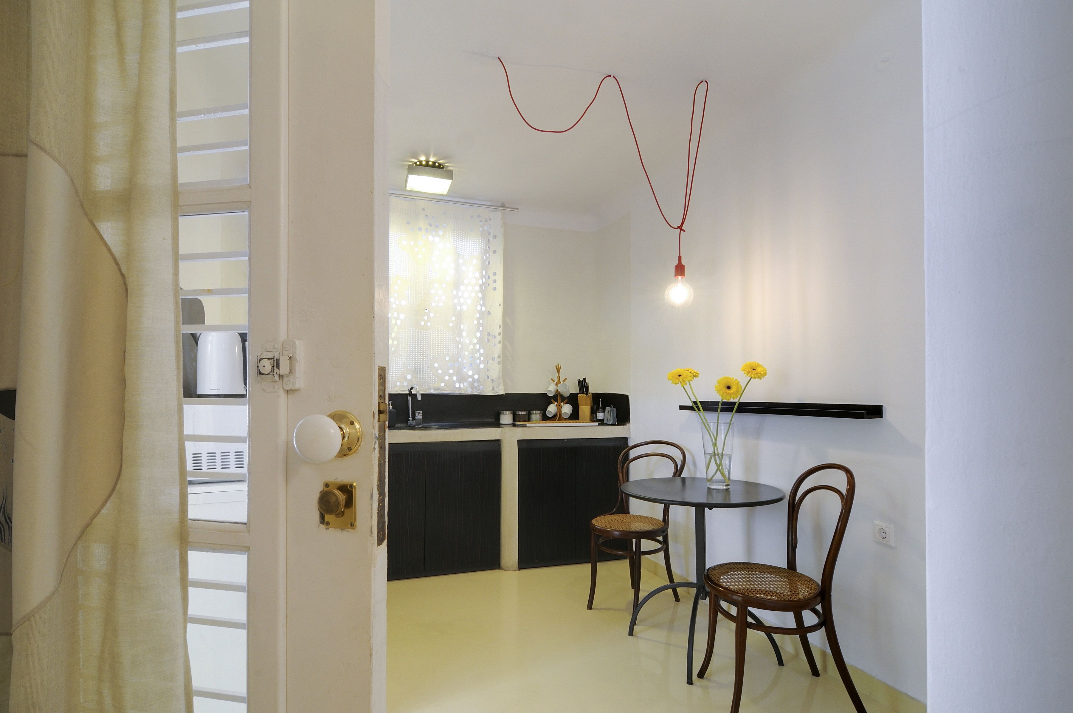 Een compacte keuken met een eethoek, met een kleine tafel en stoelen, een vaas met bloemen en een hanglamp.