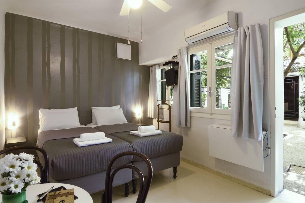 A hotel room with a bed, bedside table, chair, and a window with curtains.