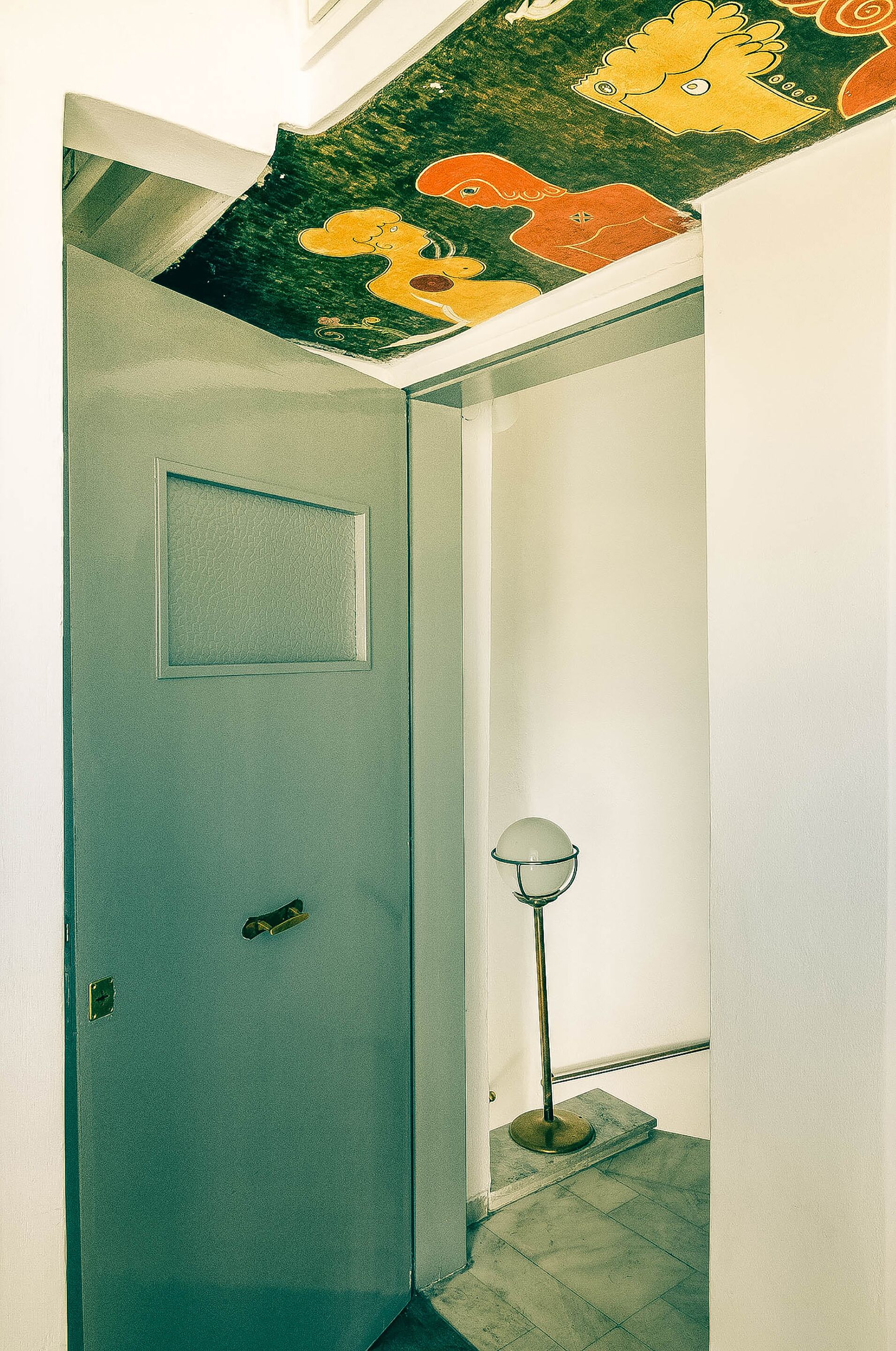 Un pasillo con una puerta, una lámpara de cristal y un techo con ilustraciones coloridas.