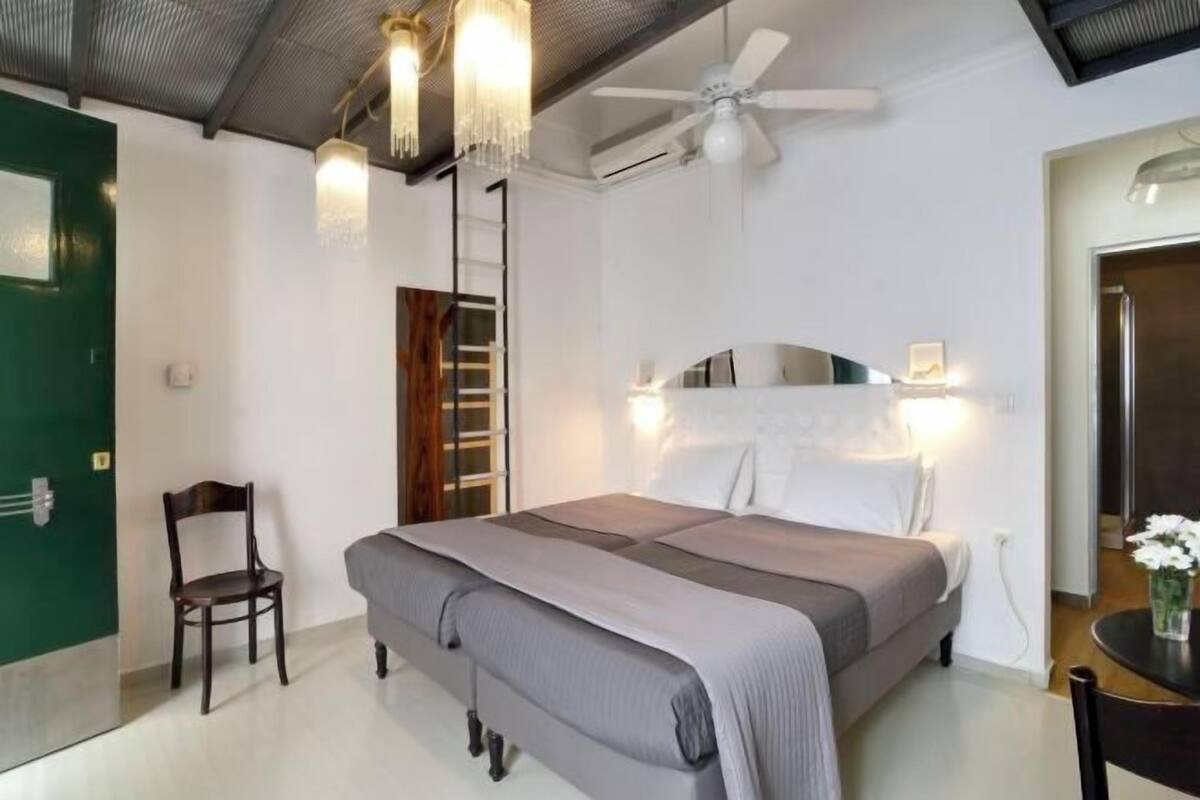 A bedroom with a bed, a chair, a desk, a ceiling fan, and a green door.