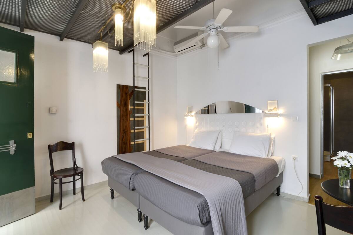 A bedroom with a bed, a chair, a desk, a ceiling fan, and a chandelier.