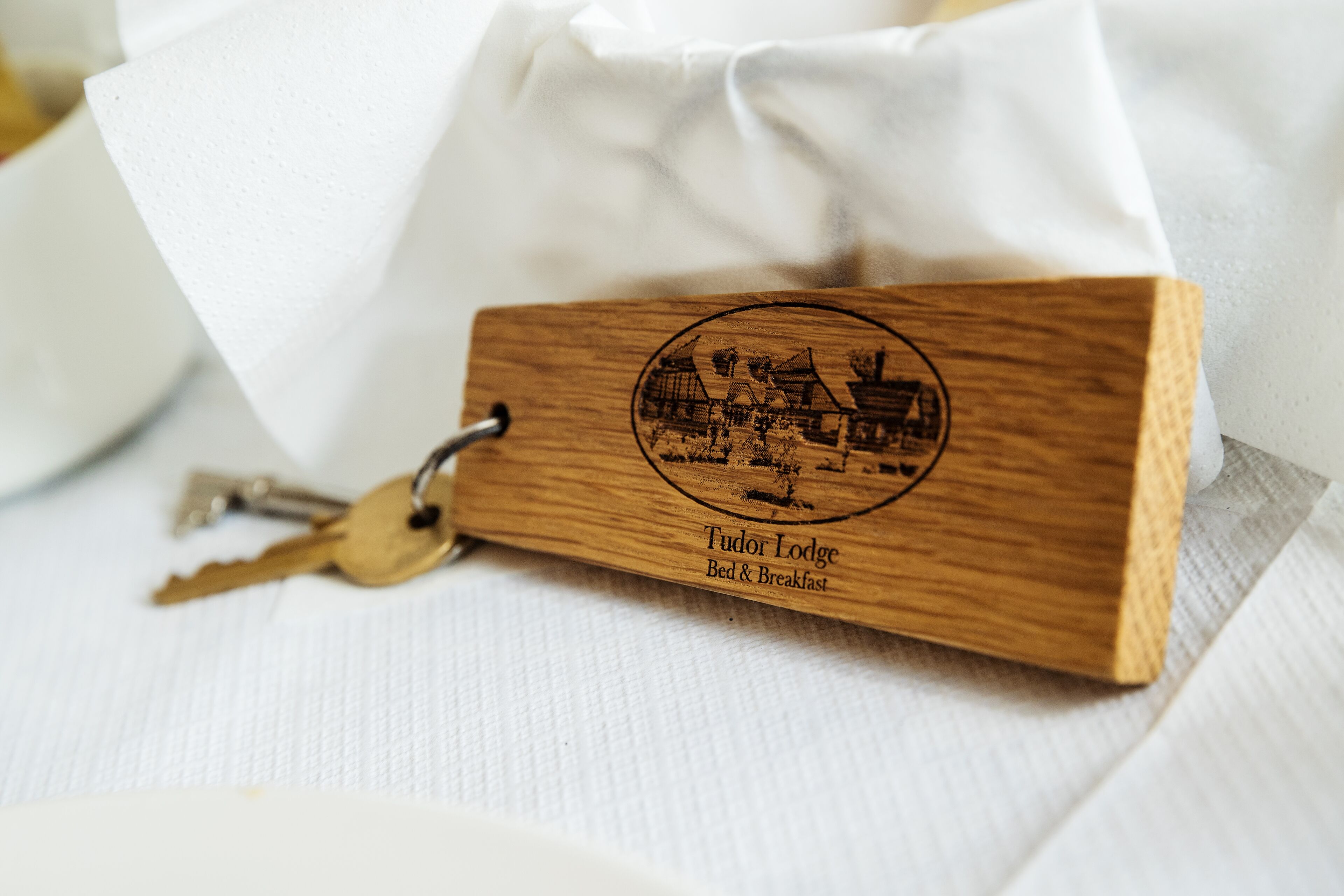 A wooden keychain with a Tudor Lodge Bed & Breakfast emblem.