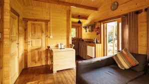 A wooden cabin interior with a dining area, kitchen, and a sofa with a patterned pillow. - Tudor Lodge (Glendalough)