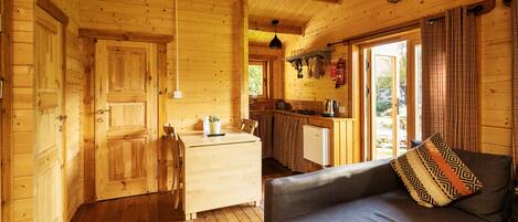 A wooden cabin interior with a dining area, kitchen, and a sofa with a patterned pillow.