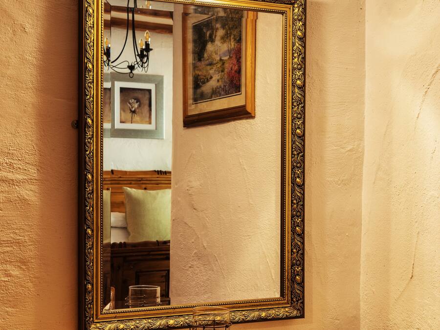 Un escritorio de madera con un espejo grande y ornamentado, una lámpara arriba y un cuadro en la pared.