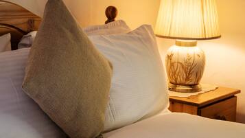 A neatly made bed with a white pillow and a brown pillow, a wooden nightstand with a lamp, and a wooden headboard.