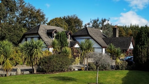 A house with a sloped roof, surrounded by a well-maintained garden with various plants and a lawn. - Tudor Lodge (Glendalough)