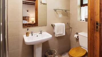 A bathroom with a sink, mirror, toilet, and a window.