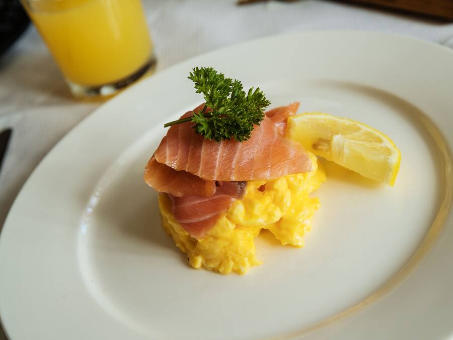 A plate with scrambled eggs topped with smoked salmon and a lemon wedge, garnished with parsley.