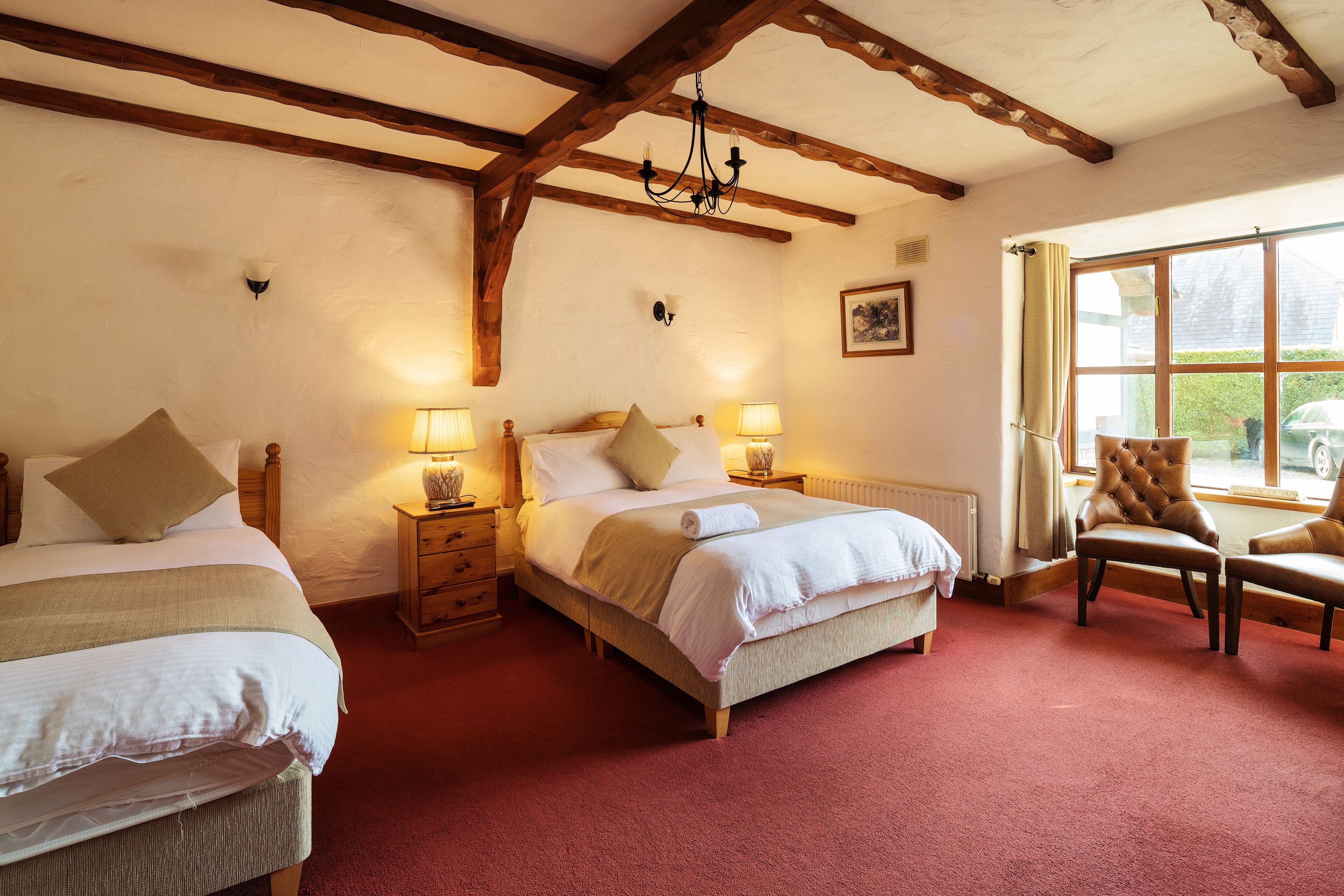 A bedroom with two beds, wooden beams, a chandelier, and a view of the outside.