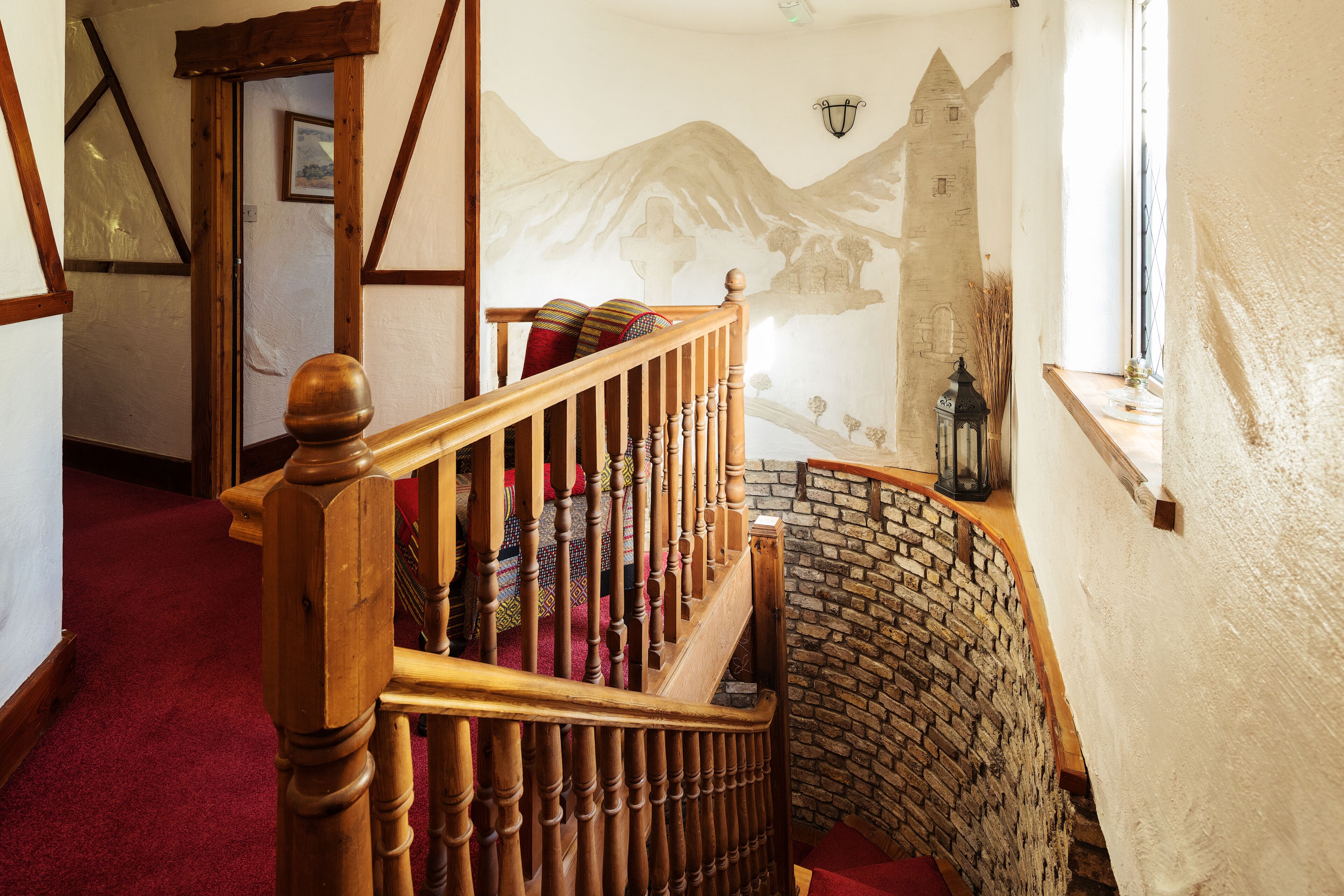 A wooden staircase with a red carpet, a stone wall, and a mural of mountains.