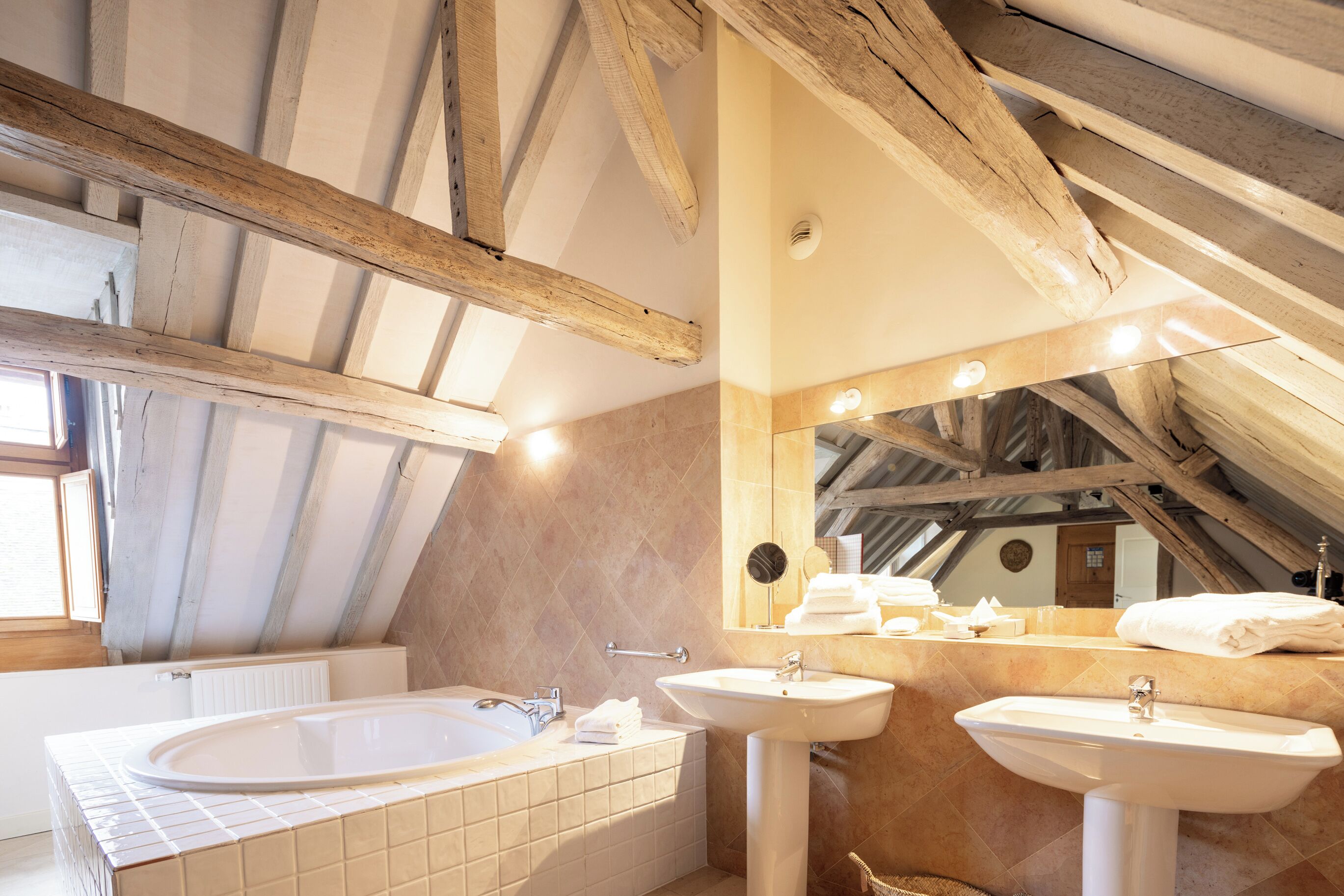 A bathroom with a bathtub, two sinks, a mirror, and wooden beams on the ceiling.