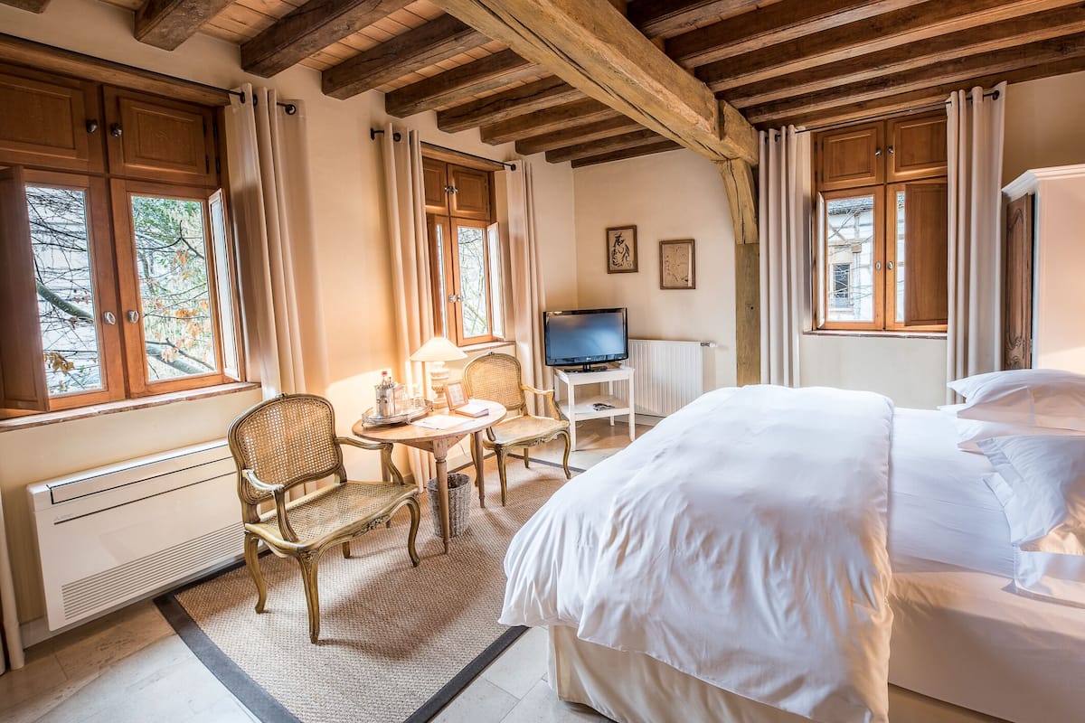 Ett hotellrum med en säng, en tv, en stol, ett litet bord och ett fönster med gardiner.