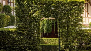 A traditional building with a prominent tower, a well-maintained garden with a hedge archway, and a stone pathway leading to the entrance. - La Maison de Rhodes Hôtel & Spa 5* (Troyes)