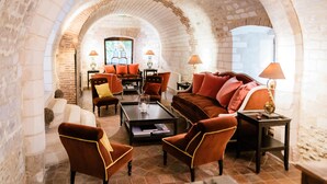 A cozy lounge area with a stone archway, comfortable seating, and a television in the background. - La Maison de Rhodes Hôtel & Spa 5* (Troyes)