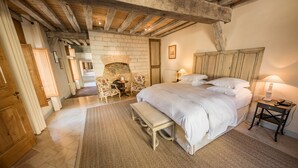 A bedroom with a large bed, a wooden headboard, a bench, a small table, and a fireplace. - La Maison de Rhodes Hôtel & Spa 5* (Troyes)