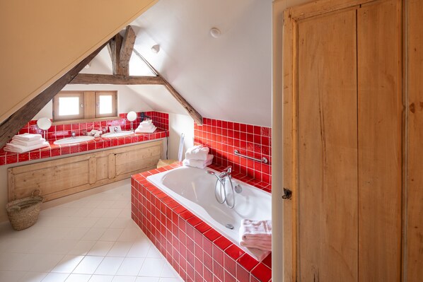 A modern bathroom with a freestanding bathtub, red tiled walls, and a wooden ceiling beam.