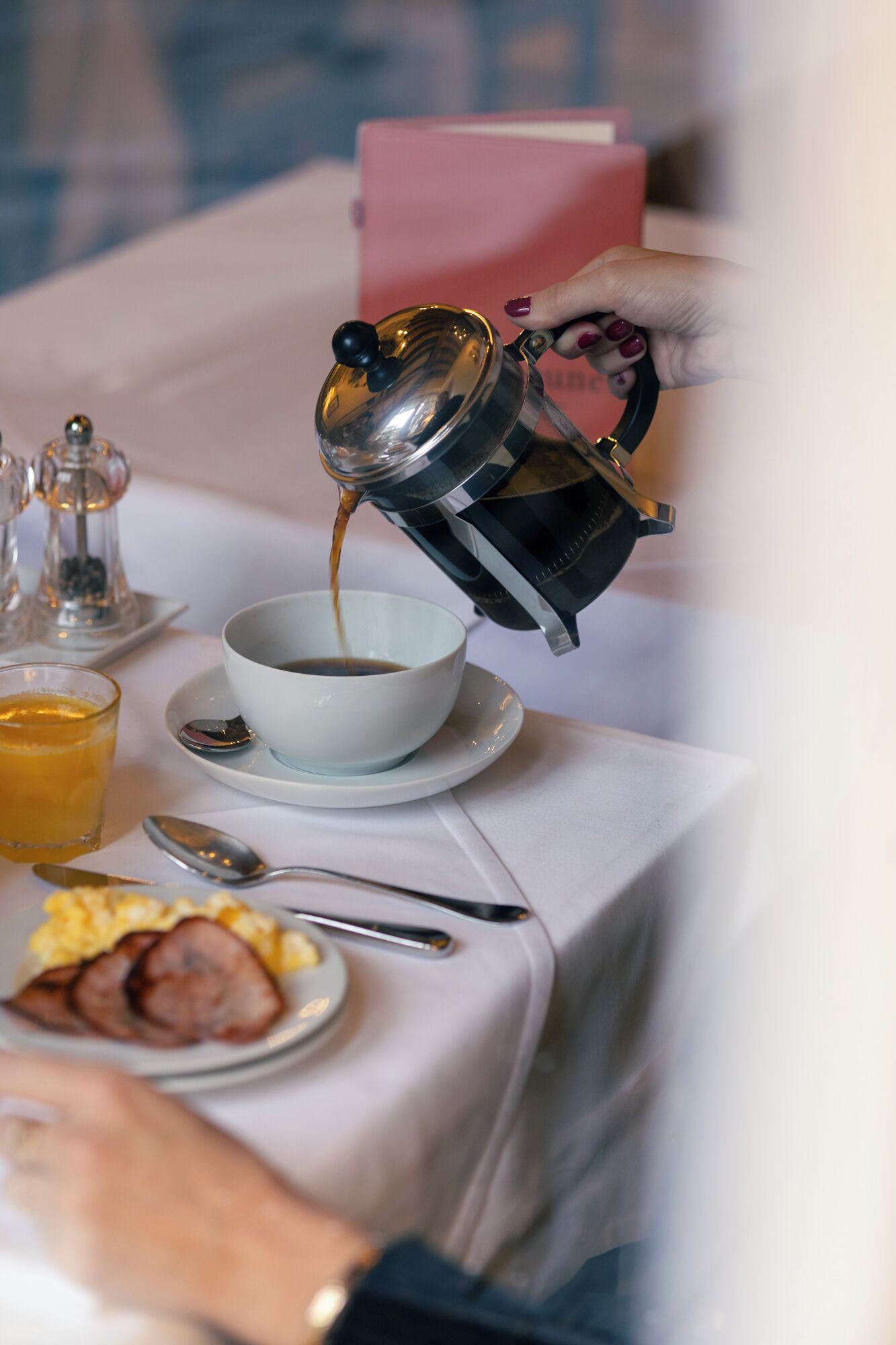 A coffee pot pouring coffee into a cup on a table with breakfast items.