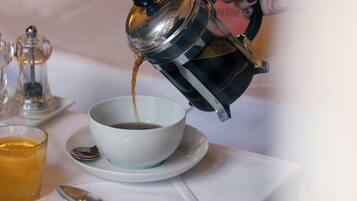 Une cafetière verse du café dans une tasse posée sur une table où se trouvent des aliments pour le petit-déjeuner.