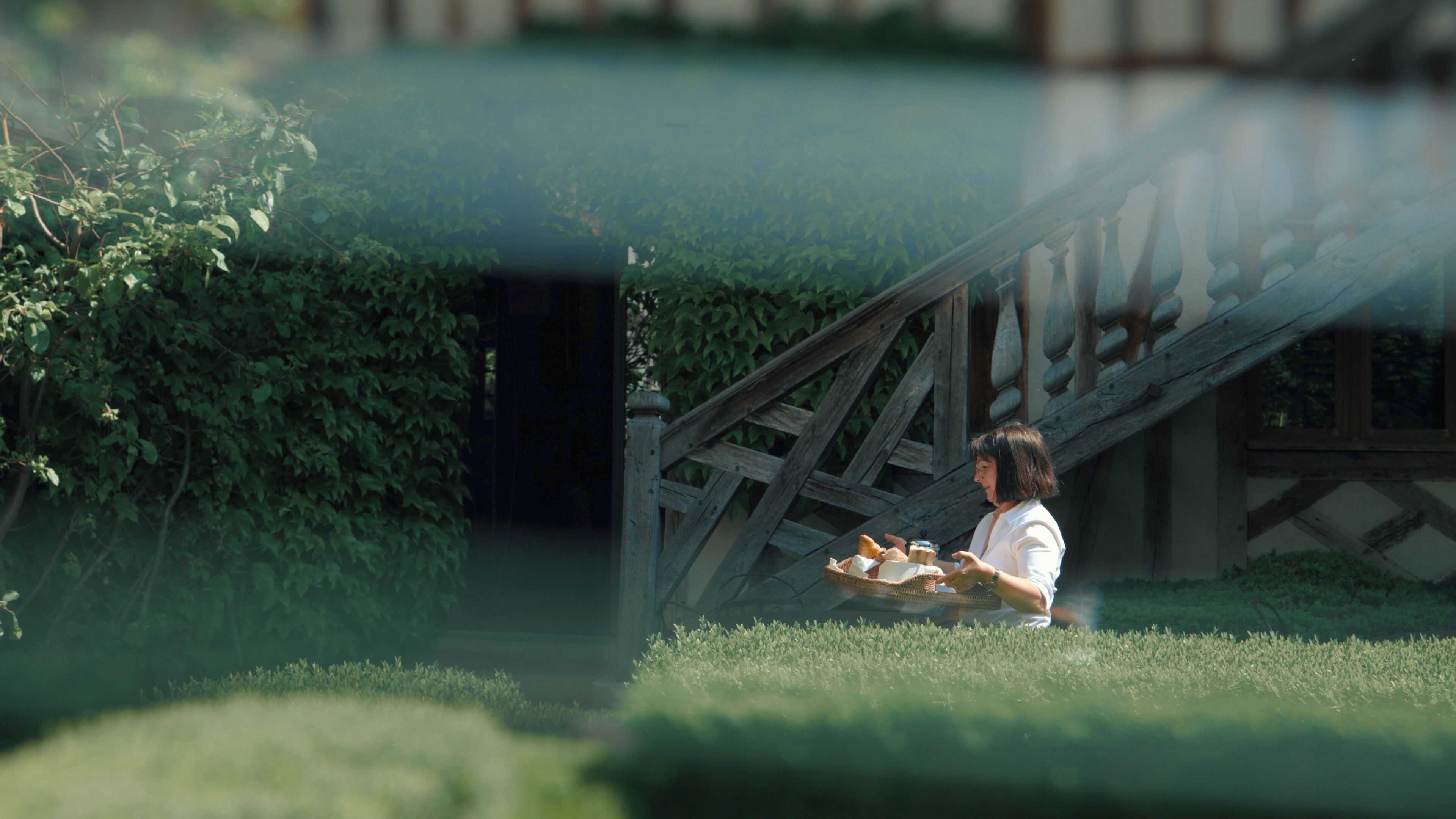A person sitting on a bench in a garden with a wooden structure in the background.
