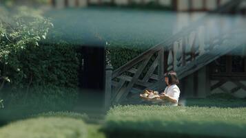 A person sitting on a bench in a garden with a wooden structure in the background.