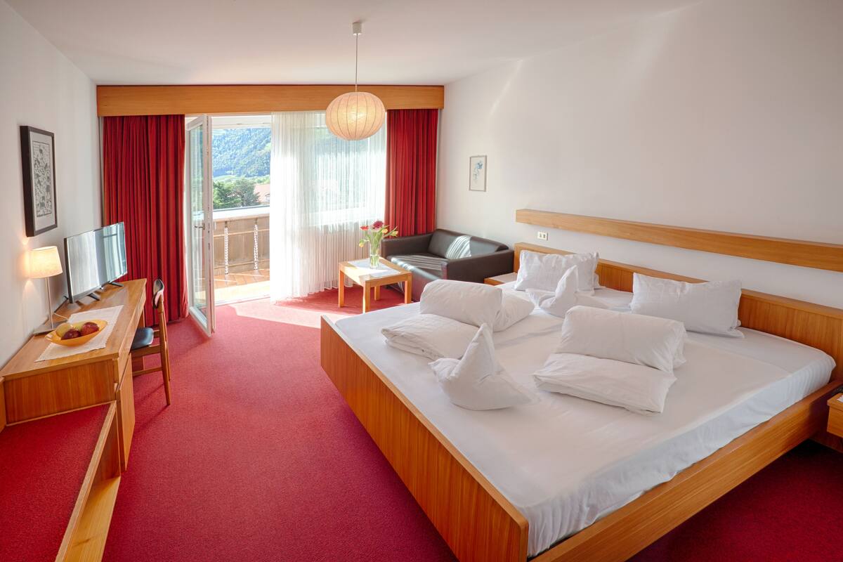 A hotel room with a large bed, a desk with a lamp, a sofa, and a view of the outdoors.