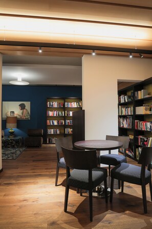 A modern library with a round table, chairs, and bookshelves. - Hotel Weingarten (Naturno)