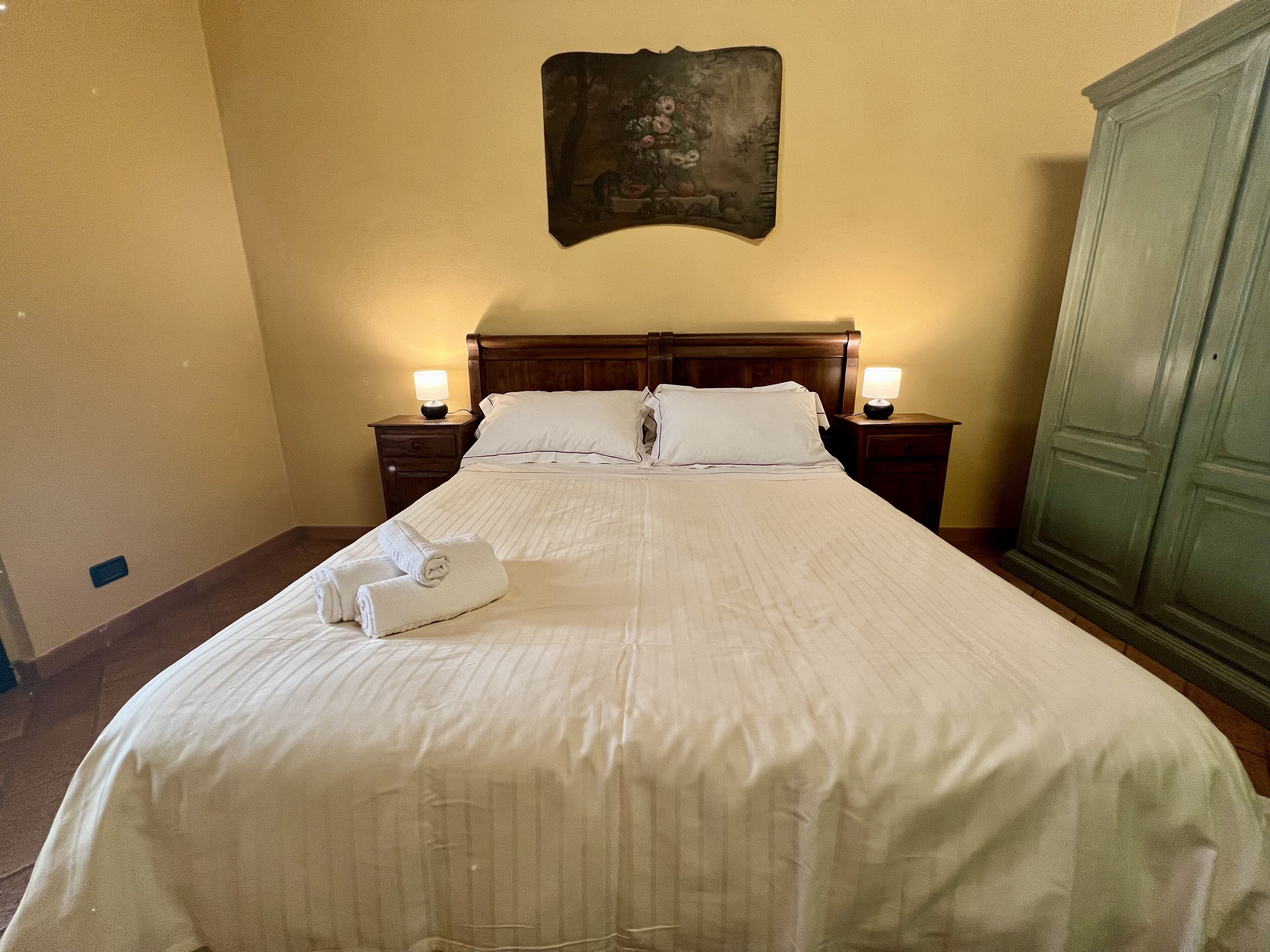 A hotel room with a large bed, two bedside tables with lamps, a wooden headboard, and a painting on the wall.