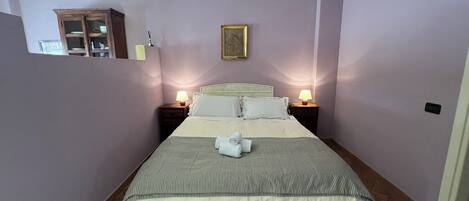A neatly made bed with a striped bedspread and pillows, two bedside lamps, a small wooden cabinet, and a framed picture on the wall.