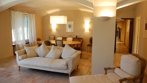 Una sala de estar con sofá, sillones, una mesa de comedor con sillas y un pasillo que conduce a otra habitación.