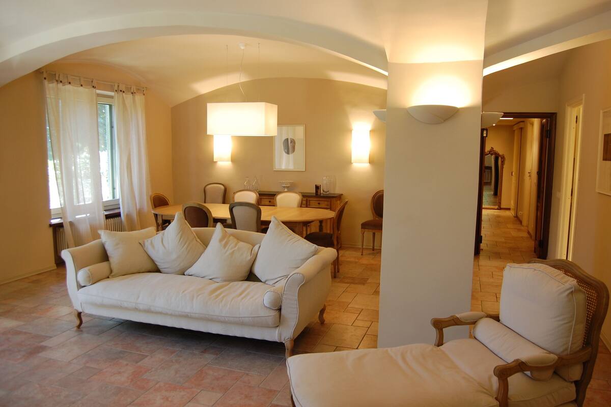 A living room with a sofa, armchairs, a dining table with chairs, and a hallway leading to another room.