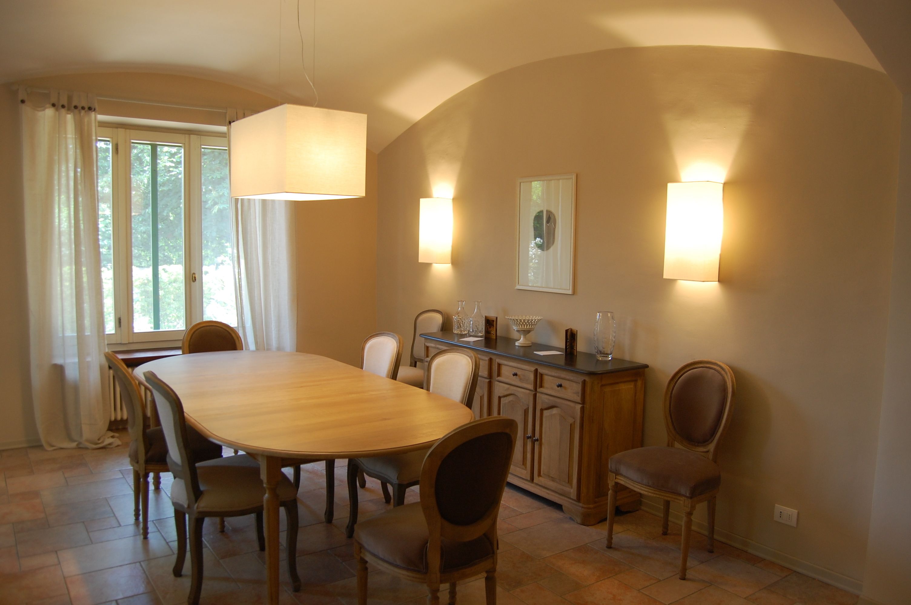 Comedor con una gran mesa de madera, seis sillas, un aparador y dos luces fijadas a la pared.