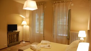 A hotel room with a bed, a television, a lamp, and a window with curtains.