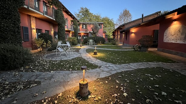 Un patio con senderos de piedra, mobiliario exterior y una chimenea central.