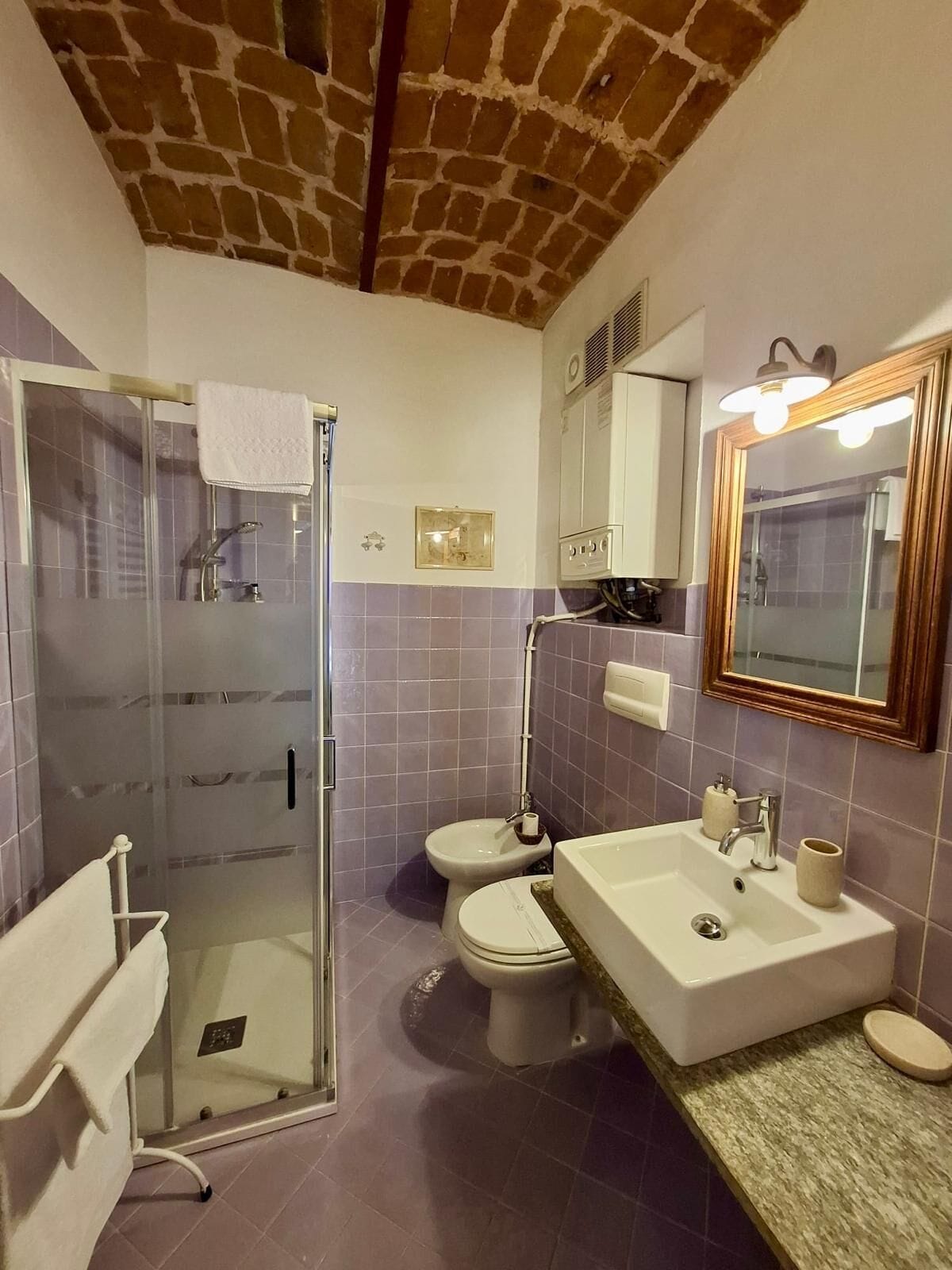 Un baño con cabina de ducha de vidrio, dos inodoros, un lavamanos y un espejo con luz.