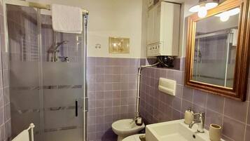 Un baño con cabina de ducha de vidrio, dos inodoros, un lavamanos y un espejo con luz.