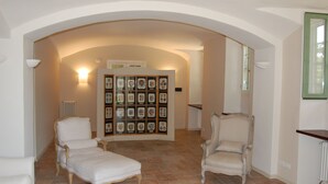 Una habitación amplia con un techo abovedado alto, dos sillones blancos, un pequeño sofá blanco y un conjunto de objetos enmarcados colgados en la pared.