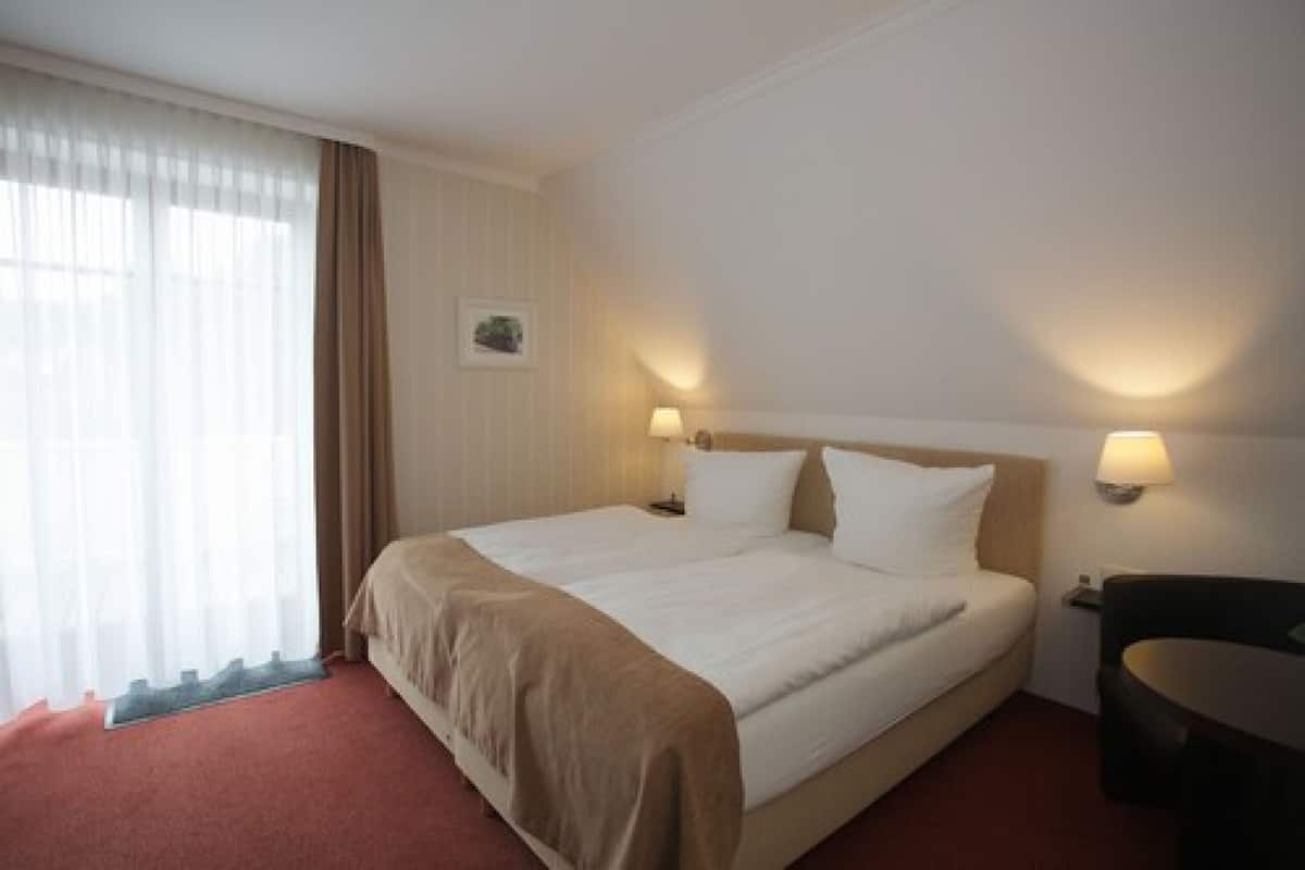 Une chambre d’hôtel avec un grand lit, deux lampes de chevet, une petite table et une fenêtre avec des rideaux.