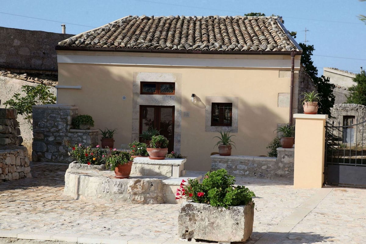 A building with a tiled roof, a stone wall, and potted plants.