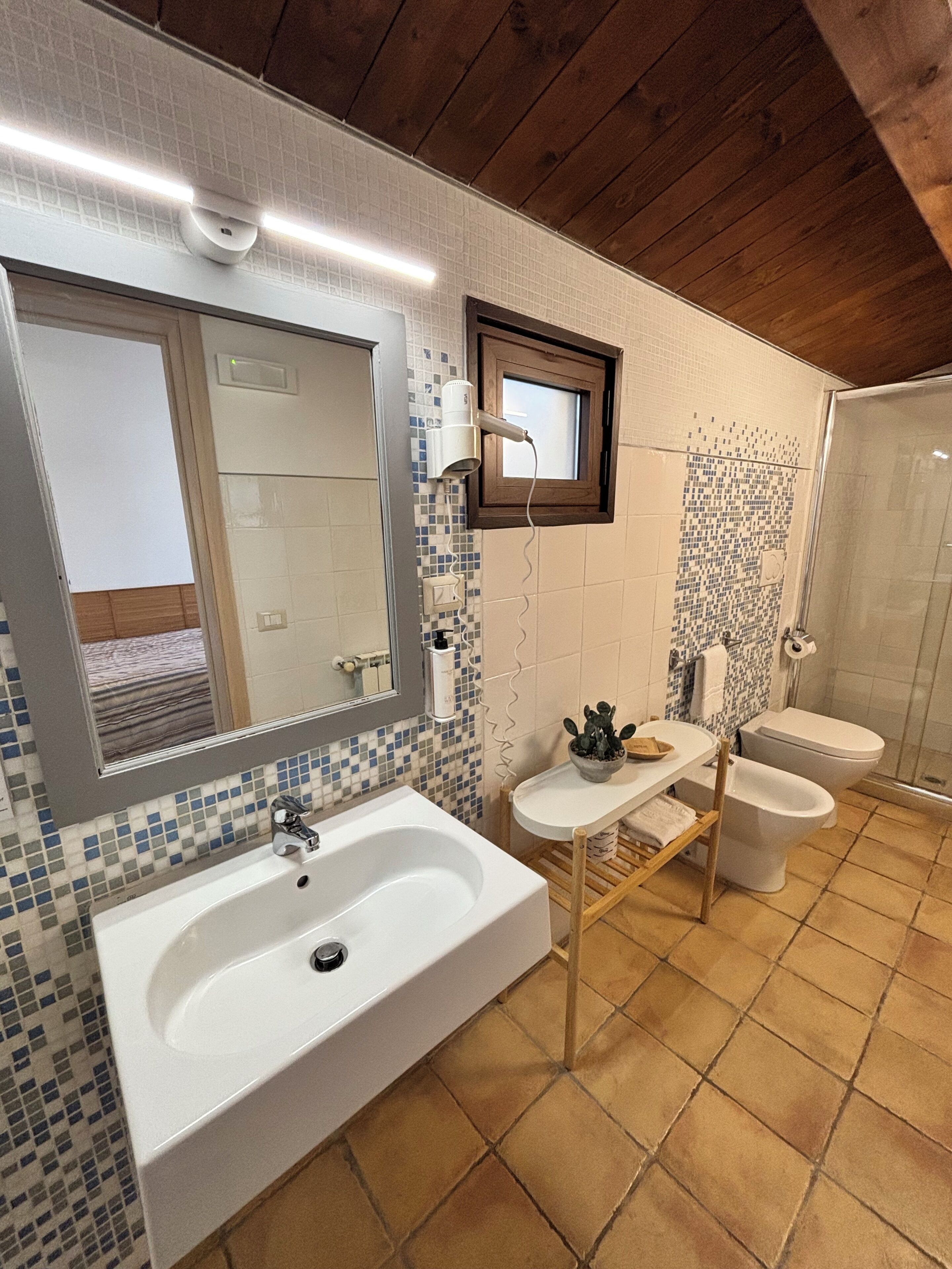 Une salle de bain avec un grand lavabo, deux toilettes, un miroir et une douche.