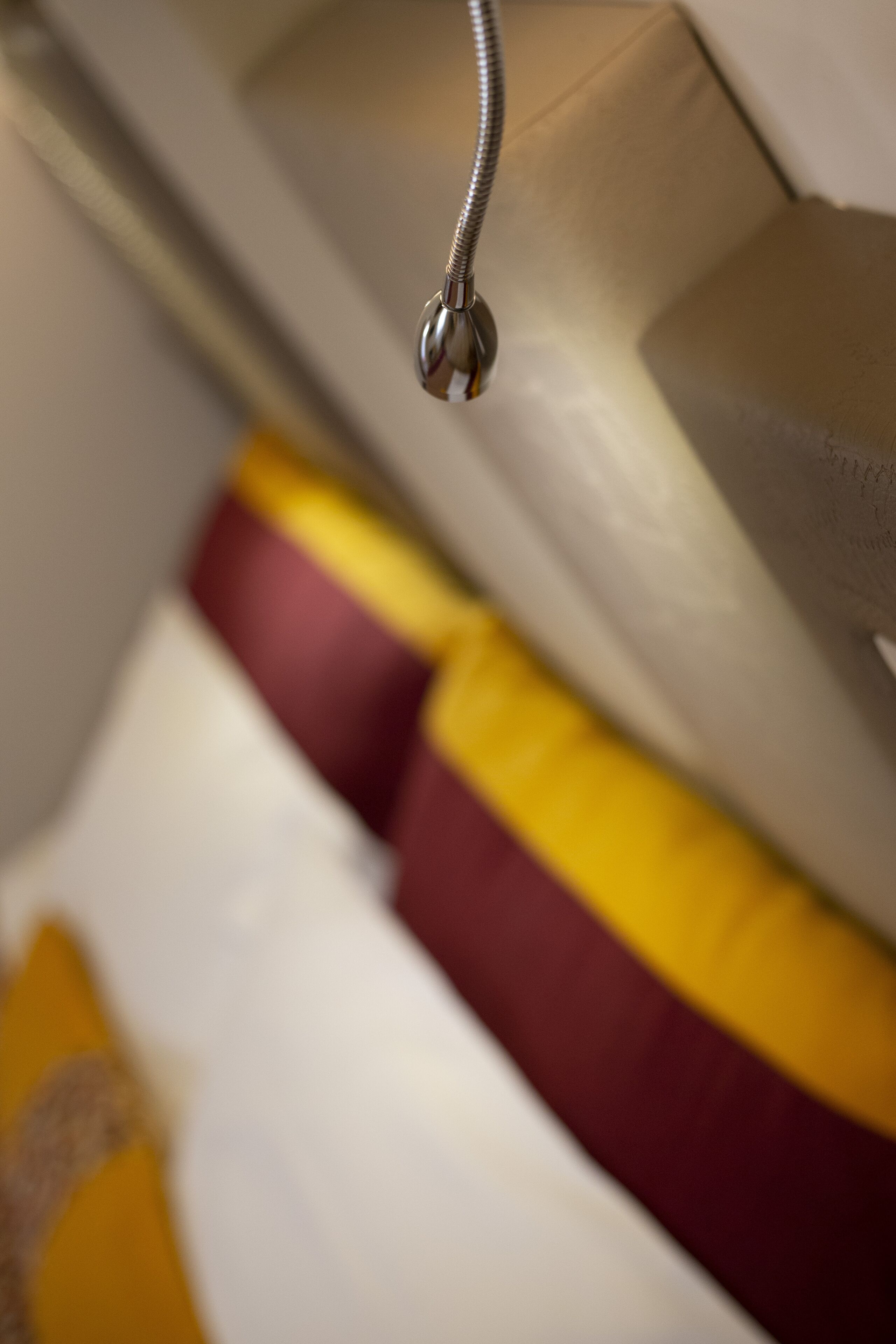 A close-up of a metallic object, possibly a part of a bed frame or furniture, with a blurred background featuring a cushion with a yellow and red pattern.