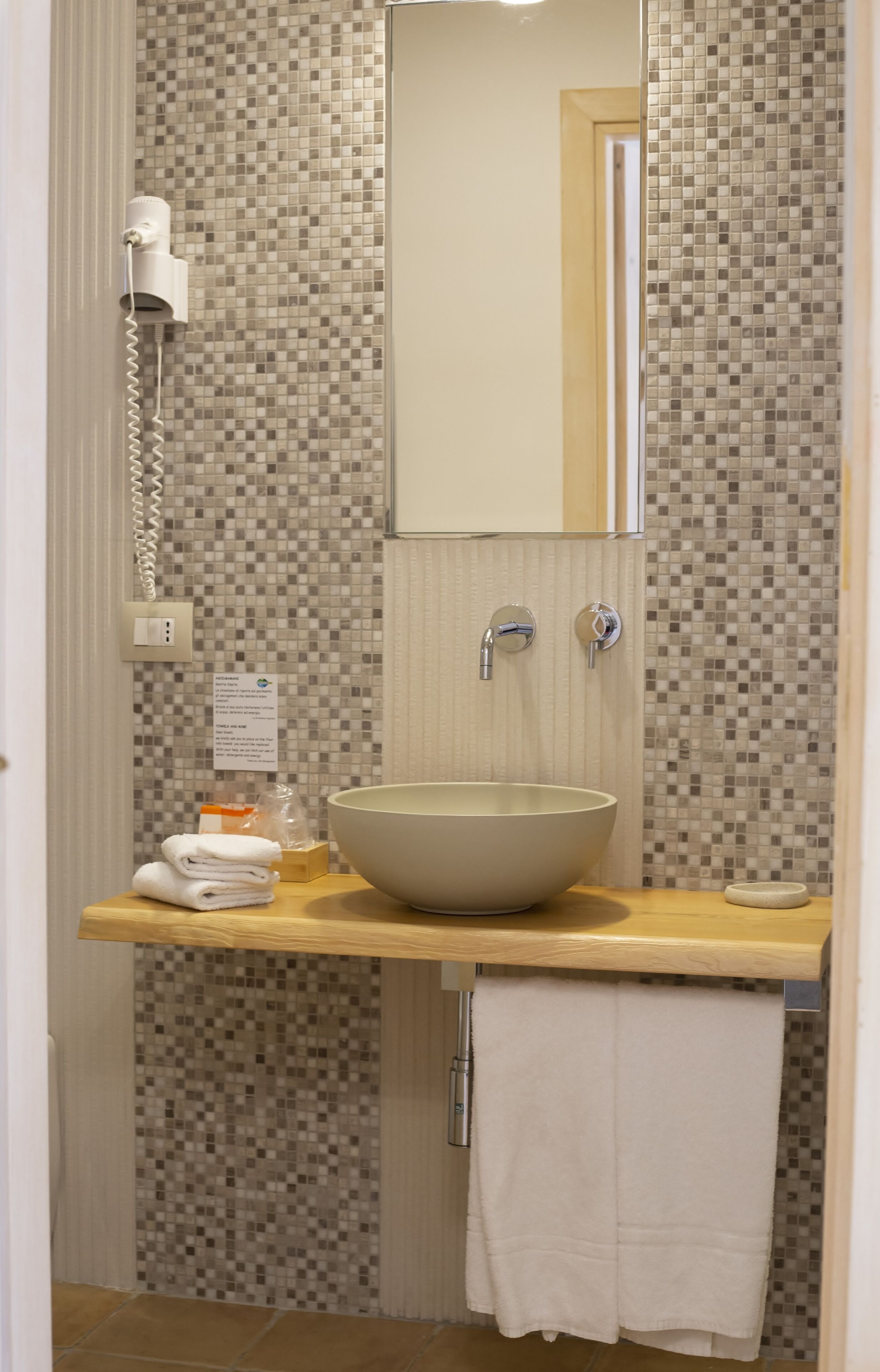 A bathroom with a tiled mosaic backsplash, a large beige sink, a mirror, a towel rack, and a hairdryer.