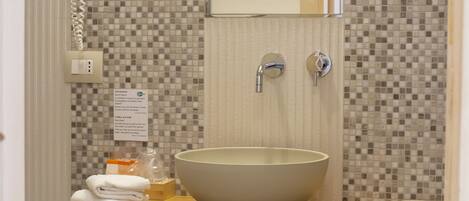 A bathroom with a tiled mosaic backsplash, a large beige sink, a mirror, a towel rack, and a hairdryer.